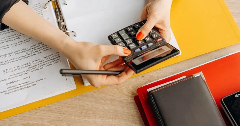 Une personne utilise une calculatrice sur un bureau avec des documents, un stylo et un agenda