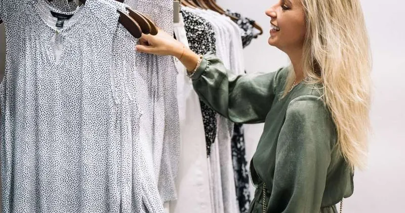 Femme blonde examine une robe blanche sur un rack dans une boutique