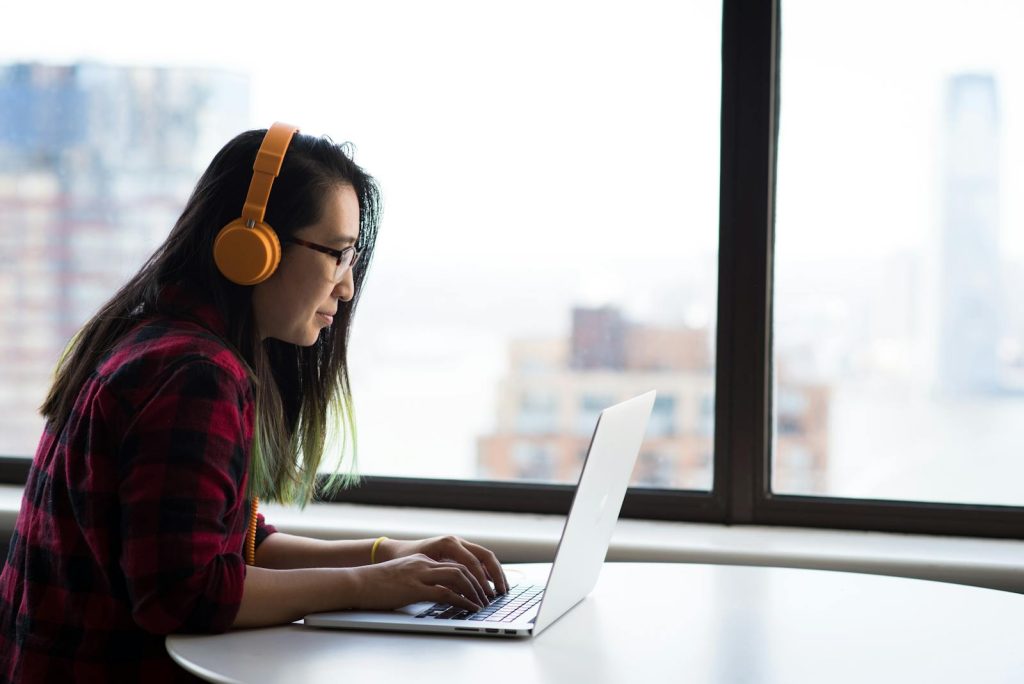 Femme asiatique avec des écouteurs utilisant un ordinateur portable pour le travail à distance dans un environnement urbain.