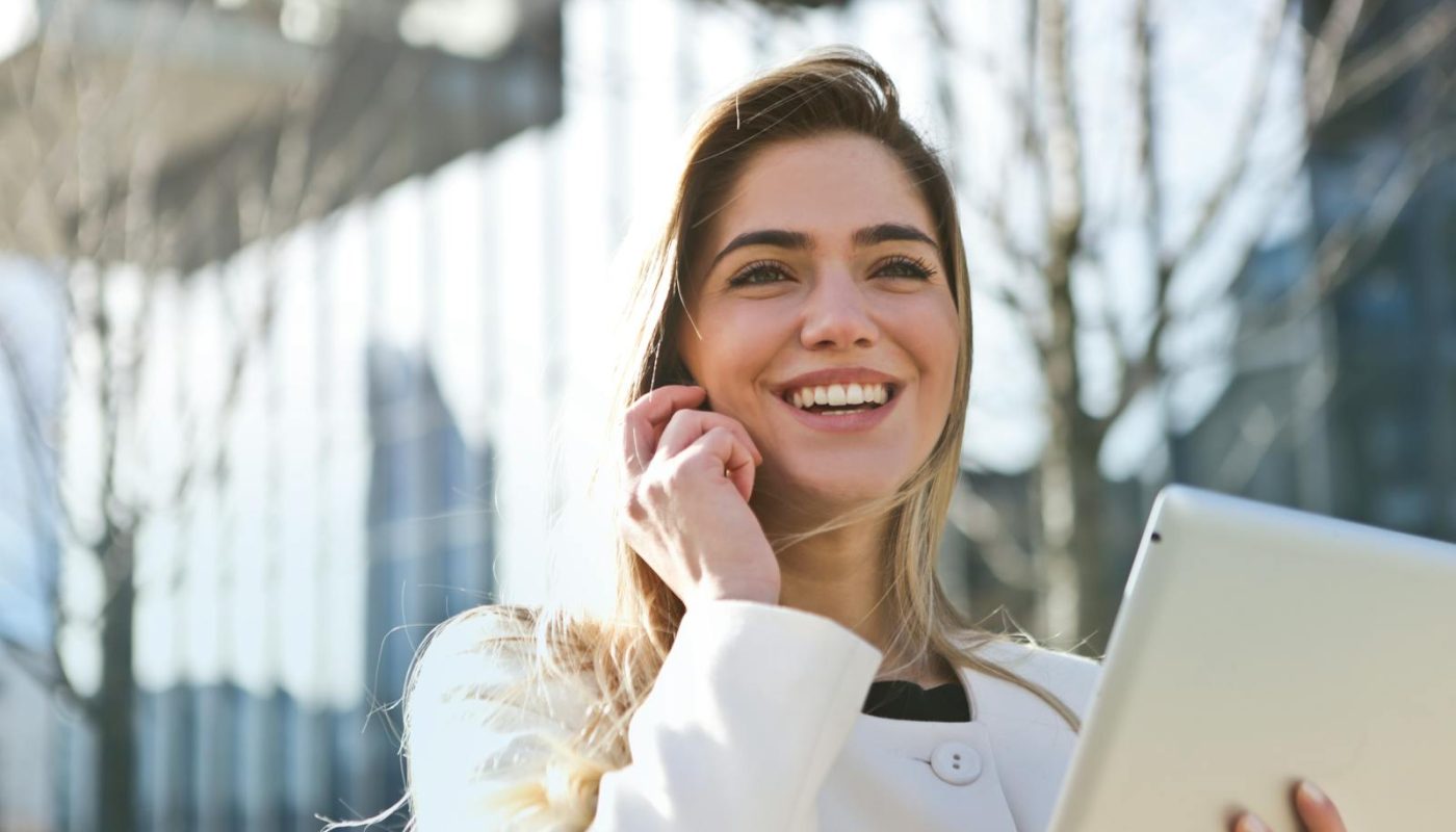 Femme d'affaires confiante utilisant sa tablette et son téléphone, souriant à l'extérieur en plein soleil.