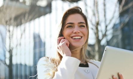 Femme d'affaires confiante utilisant sa tablette et son téléphone, souriant à l'extérieur en plein soleil.